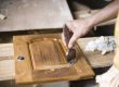 Close-up of a hand applying a wood finish to a cabinet panel in a workshop