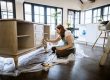 Woman restoring a wooden sideboard in a bright, modern home with large windows
