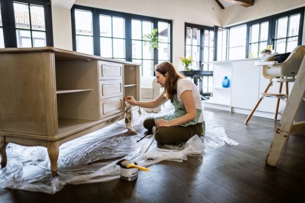 Woman restoring a wooden sideboard in a bright, modern home with large windows