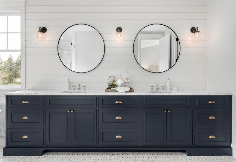 A stylish bathroom featuring two mirrors and a dark blue vanity, showcasing cabinets from Portland, OR